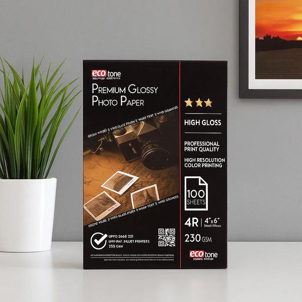 Box of eco-tone Premium Glossy Photo Paper on a surface with a plant and framed picture in the background.