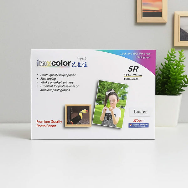 Box of imacolor photo paper with a child in a park on the cover, placed on a white surface with a plant in the background.
